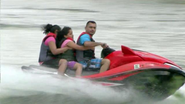 A man carries a woman and child on a watercraft on the Rio Grande. 