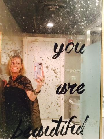Amanda Lamb captures a selfie in a restroom where "You Are Beautiful" is stenciled on the mirror.