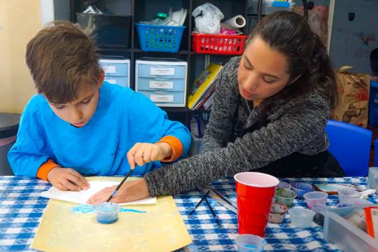 Andrea, Director of Programming, helps camper Daniel paint a bluebird. The artwork will be auctioned off at the non-profit's annual fundraiser, the Bluebird Ball.