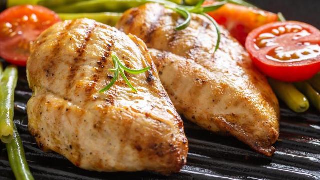 Barbecued chicken breasts on a grill pan with fresh green vegetable and chery tomatoes and rosemary twigs.