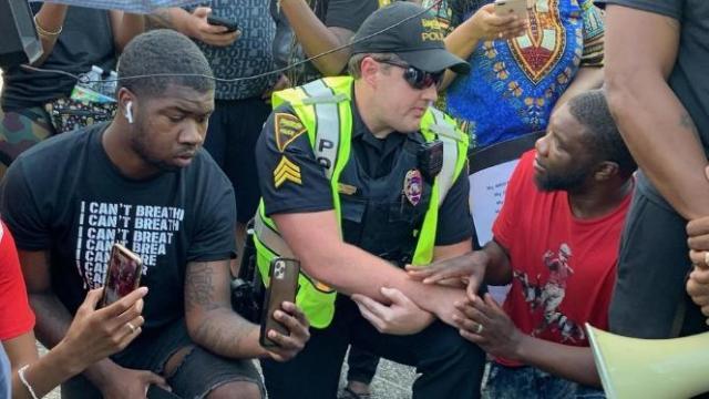 A Fayetteville police officer kneels with protestors. Credit: Fayetteville Observer