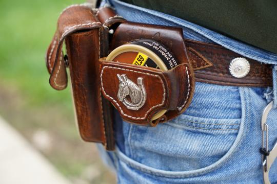 Tobacco dip sits on Cowboy's hip, in a leather holster featuring a horseshoe. 