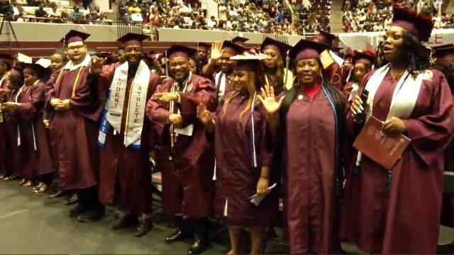 NCCU graduates walk across the stage, some in borrowed caps and gowns