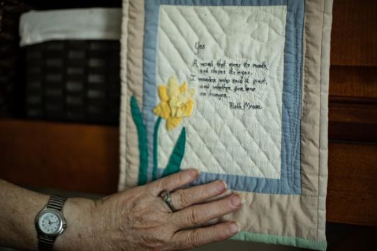 Ruth Moose gestures to a gifted piece of quilt on which a friend stitched one of her poems.
