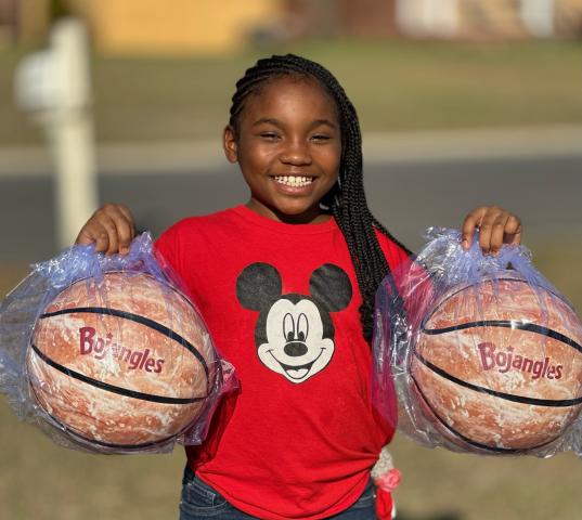 A young girl holds up two Bojagnles biscuit-shaped basketballs.